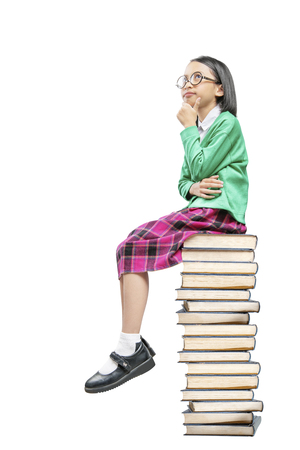 Asian cute girl with glasses think while sitting on the pile of books isolated over white background. Back to School conceptの写真素材
