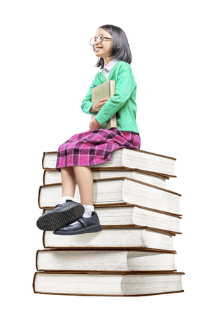 Asian cute girl with glasses holding the book while sitting on the pile of books isolated over white background. Back to School conceptの写真素材