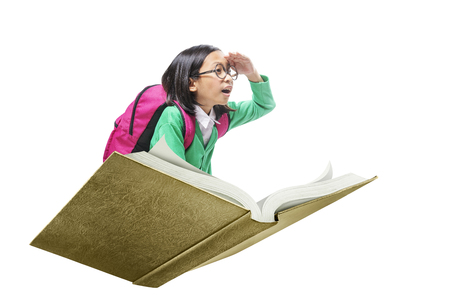 Asian cute girl with glasses and backpack sitting on book isolated over white background. Back to School conceptの写真素材
