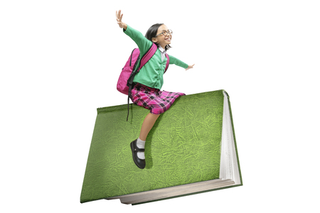Asian cute girl with glasses and backpack sitting on book isolated over white background. Back to School conceptの写真素材