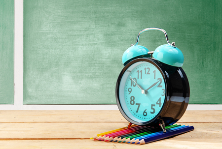 Alarm clock and colored pencils on wooden table with chalkboard background. Back to School conceptの写真素材