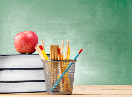 Pile of books with apple and pencils in basket container on wooden table with chalkboard background. Back to School conceptの写真素材