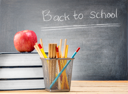 Pile of books with apple and pencils in basket container on wooden table and blackboard with Back to School message. Back to School conceptの写真素材