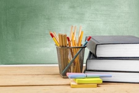 Pile of books with notes paper and pen with pencils in basket container on wooden table with chalkboard background. Back to School conceptの写真素材