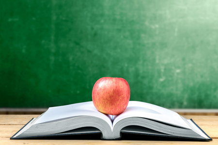 Apple on the middle of opened book on wooden table with chalkboard background. Back to School conceptの写真素材