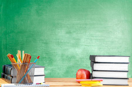 Pile of books with notes paper and pen, apple and pencils in basket container on wooden table with chalkboard background. Back to School conceptの写真素材