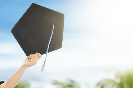 Hand holding graduation hat with blue sky background. Graduation conceptの写真素材