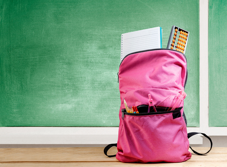 Pink backpack with book and different stationery on the wooden table with chalkboard background. Back to School conceptの写真素材