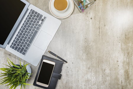 Top view of business desk with laptop, mobile phone, coffee, potted plant, notebook and business accessories on the officeの写真素材