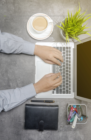 Top view of businessman working using laptop with coffee, potted plant, notebook and business accessories on the deskの写真素材