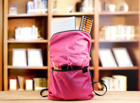 Pink backpack with book and different stationery on the wooden table in library. Back to School conceptの写真素材