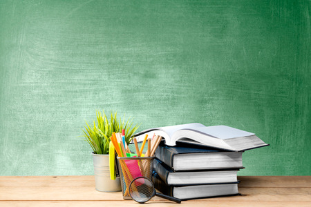 Pile of books with potted plant and pencils in basket container with magnifying glass on the wooden table with chalkboard background. Back to School conceptの写真素材