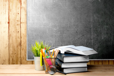 Pile of books with potted plant and pencils in basket container with magnifying glass on the wooden table with blackboard background. Back to School conceptの写真素材