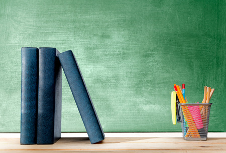 Pile of books standing and pencils in basket container with green stapler on the wooden table with chalkboard background. Back to School conceptの写真素材