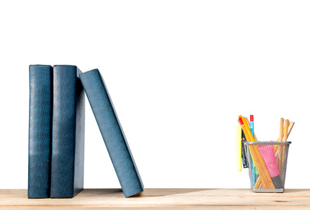 Pile of books standing and pencils in basket container with green stapler on wooden table isolated over white background. Back to School conceptの写真素材