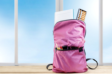 Pink backpack with book and different stationery on the wooden table with window glass background. Back to School conceptの写真素材