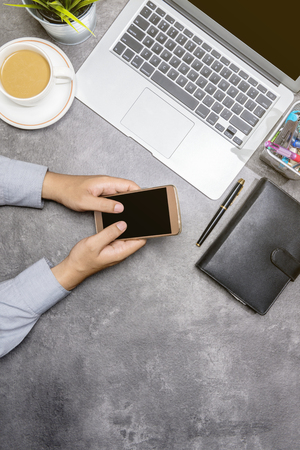 Top view of businessman using mobile phone with laptop, coffee, potted plant, notebook and business accessories on the office deskの写真素材