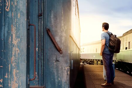 Rear view of asian man with suitcase bag and backpack standing and waiting a train on station with blue sky backgroundの写真素材