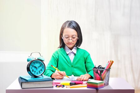 Asian cute girl in glasses learning with school stationary on the desk in classroomの写真素材