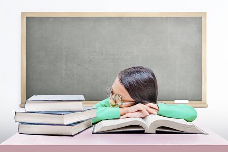 Asian cute girl with glasses fall asleep on book on the desk with chalkboard backgroundの写真素材