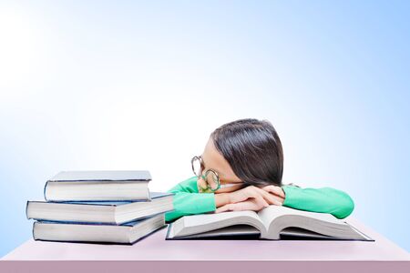 Asian cute girl with glasses fall asleep on book on the desk over bright backgroundの写真素材