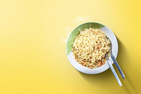 Noodles on the bowl with spoon and fork on yellow backgroundの写真素材