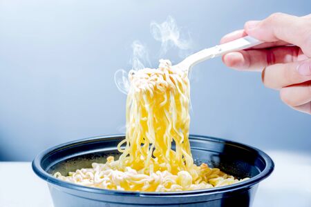 People eat the noodles with fork over bright background