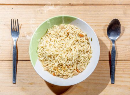 Noodles on the bowl with spoon and fork on wooden table backgroundの写真素材