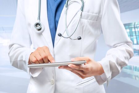 Woman doctor in white lab coat and stethoscope using tablet on the hospitalの写真素材