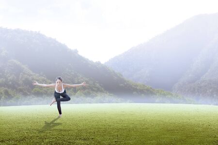 Asian healthy woman practicing yoga on the green grass field with mountains backgroundの写真素材