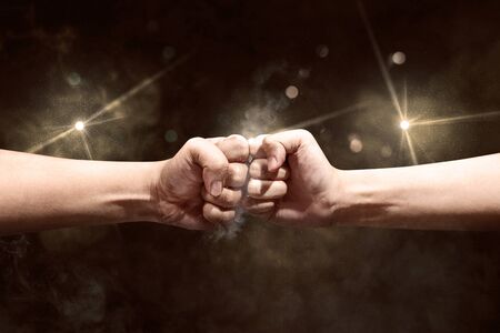 Hands of two men bumped their fists over bright lights background