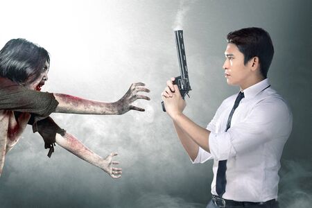 Asian businessman with the gun on his hand face the zombies amid the fog. Halloween conceptの写真素材