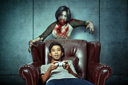 Scary zombies haunted Asian men while playing games on the couch at home. Halloween conceptの写真素材