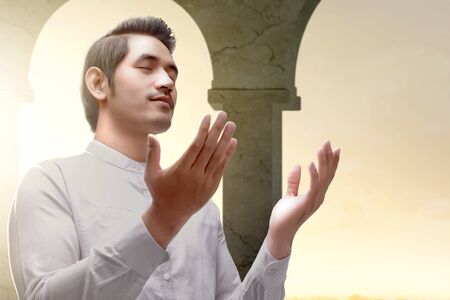 Asian Muslim man standing and praying while raised arms inside the mosqueの写真素材