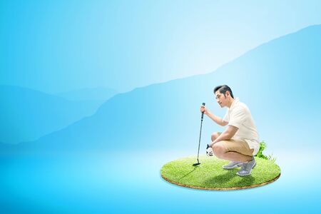 Asian man with putter golf crouching and look at a distance on the green golf courseの写真素材