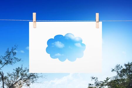 Paper with a piece of cloud pattern hanging on the rope with a paper clip over a branch of trees and blue sky backgroundの写真素材