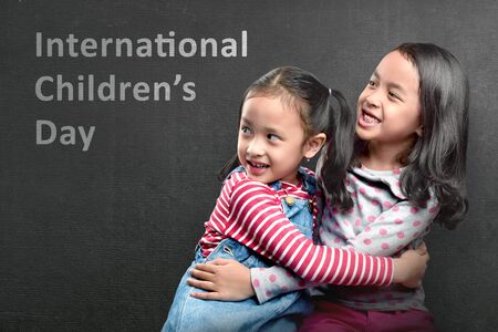 Two Asian cute girls hugging with black wall background. International Children Dayの写真素材