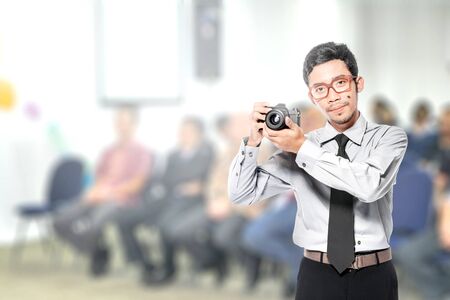 Asian businessman holding the camera on his hand standing on the officeの写真素材