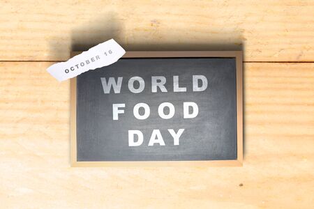 Chalkboard with World Food Day text and ripped paper with the date of October 16 on a wooden background. World Food Dayの写真素材