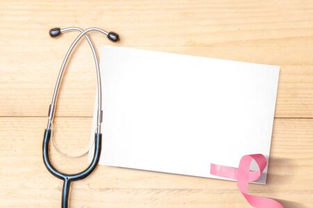 Pink awareness ribbon and stethoscope with empty white paper on a wooden background. Breast cancer awarenessの写真素材