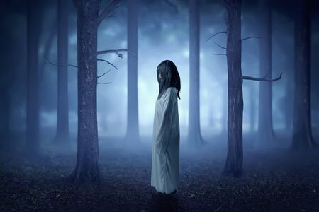 Scary ghost woman with blood and dirty face standing in the haunted forest with fog and moonlight. Halloween conceptの写真素材