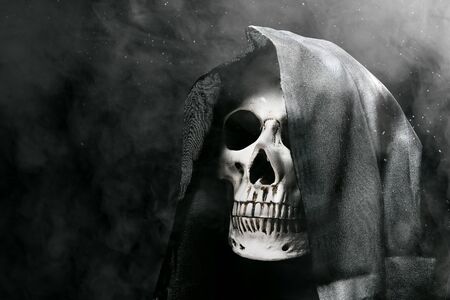 Human skull with a black cloak over a dark smoke background