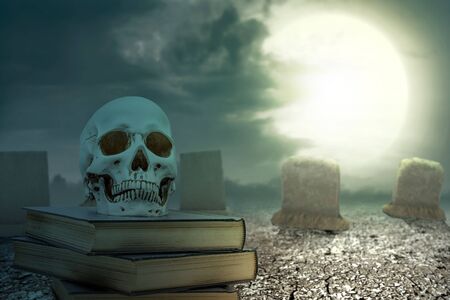 Pile of the book with a human skull on the cracked ground with tombstone and moonlight background
