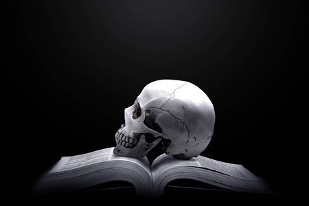 Opened book with a human skull on the table over dark backgroundの写真素材