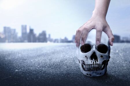 Hand holding human skull on the urban street with the night scene backgroundの写真素材