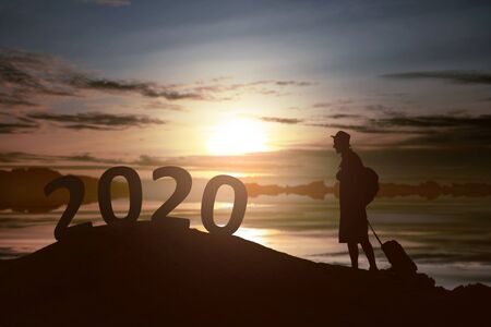 Silhouette of traveler man with a suitcase sees 2020 on the top of the hills with a sunset sky background. Happy New Year 2020の写真素材
