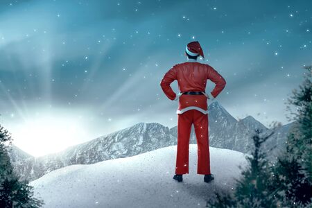 Rear view of an Asian man in Santa costume standing with snowy trees and sunlight backgroundの写真素材