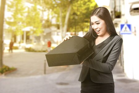 Asian businesswoman opening the black shopping bags in the city. Black Friday concept
