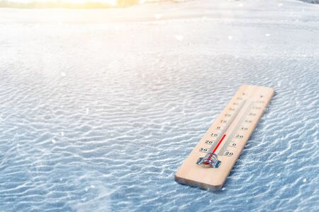 Wooden thermometer with the low temperature at winter with snowfall background