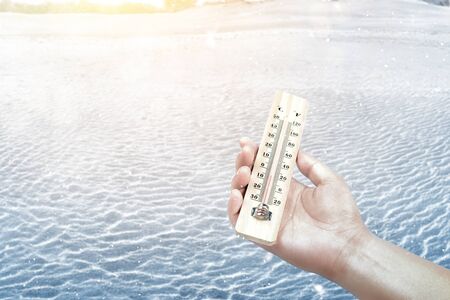 Hands holding the thermometer with the low temperature at winter with snowfall background